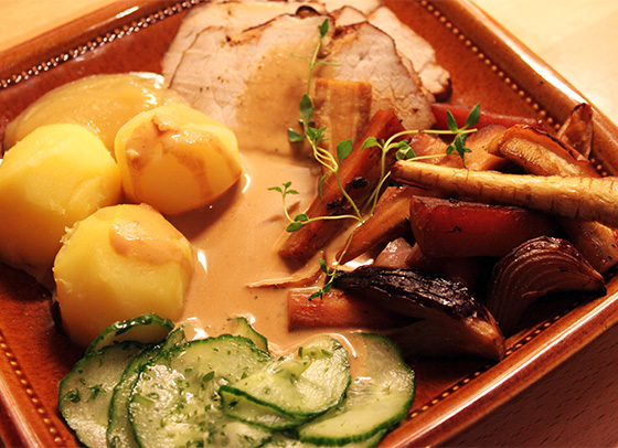 Helstekt kotlettrad i skivor, serverad med ugnsrostade rotfrukter och äpplen, kokt potatis, pressgurka, sås och äppelmos.
